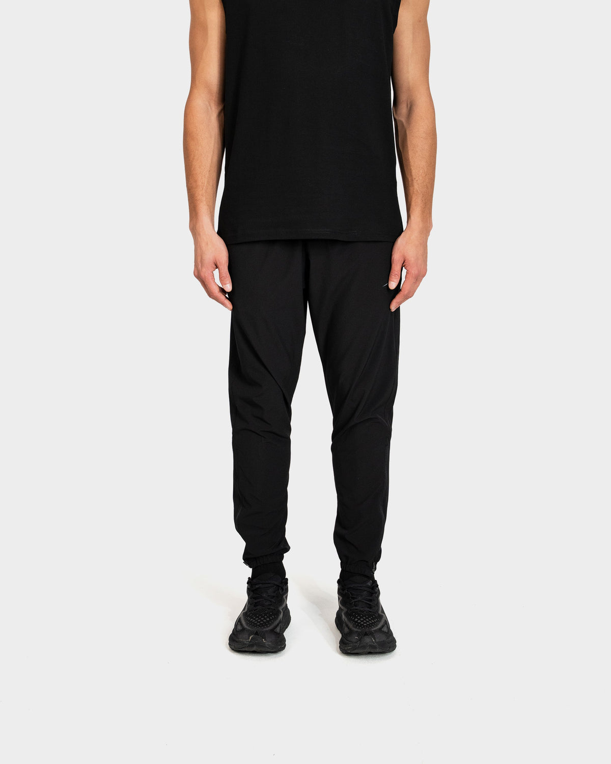 Person wearing a black sleeveless top and black Deenathletic pants on a white background