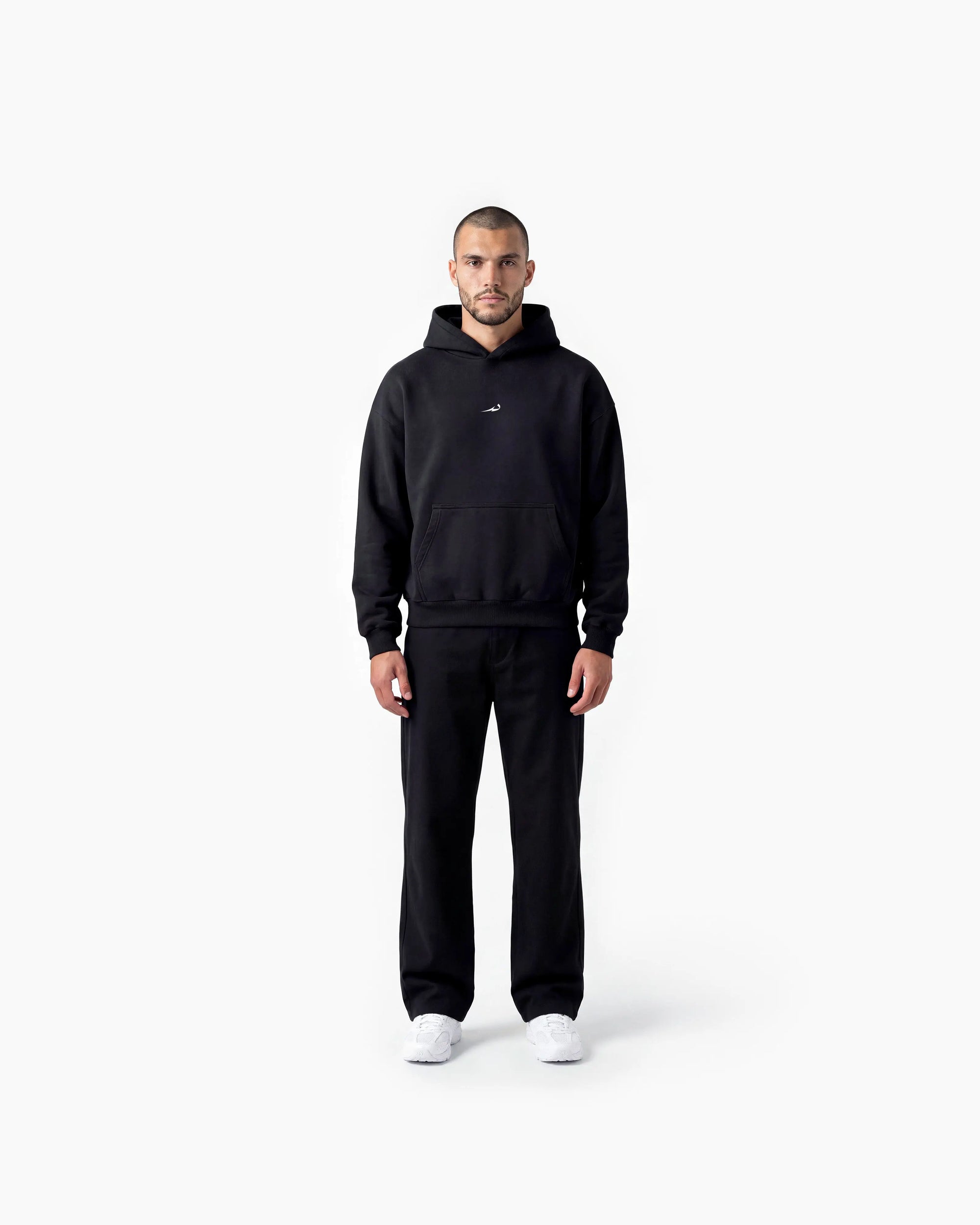 A man modeling a black Deenathletic pullover hoodie and matching black sweatpants against a clean white studio background.